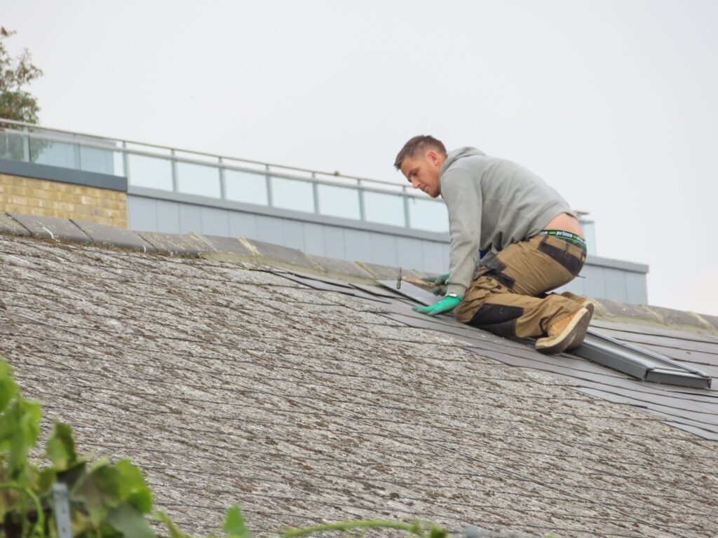 Roofing contractor installing shingle tiles on a sloped residential roof in direct sunlight